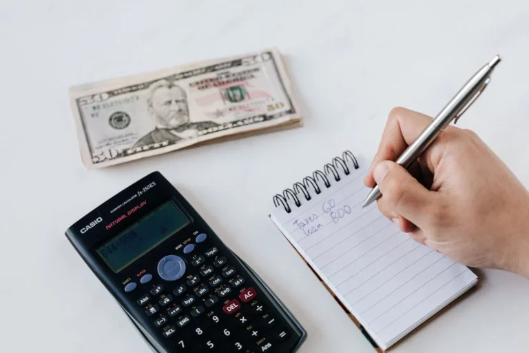 A table with a calculator, a twenty dollar bill and a notepad