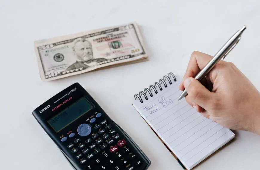 A table with a calculator, a twenty dollar bill and a notepad