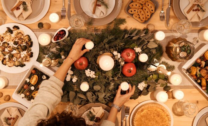 A bird's eye view of a holiday dinner table with garland in the middle and shared dishes around the edge
