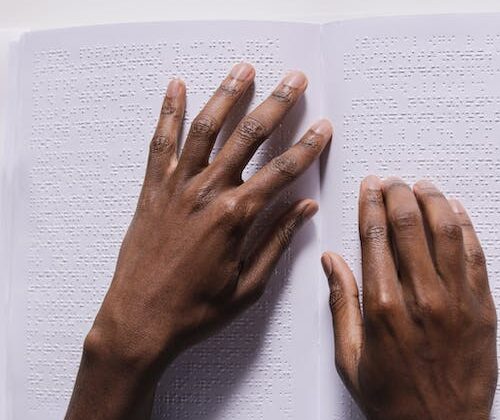 Two hands reading a braille book on a white table