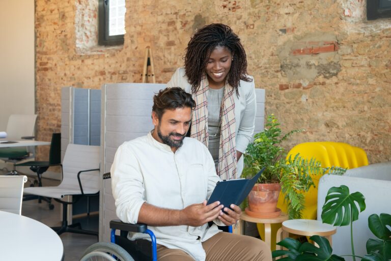 A man using a wheelchair and a woman smile at an iPad screen
