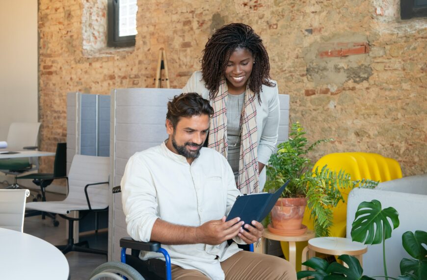 A man using a wheelchair and a woman smile at an iPad screen