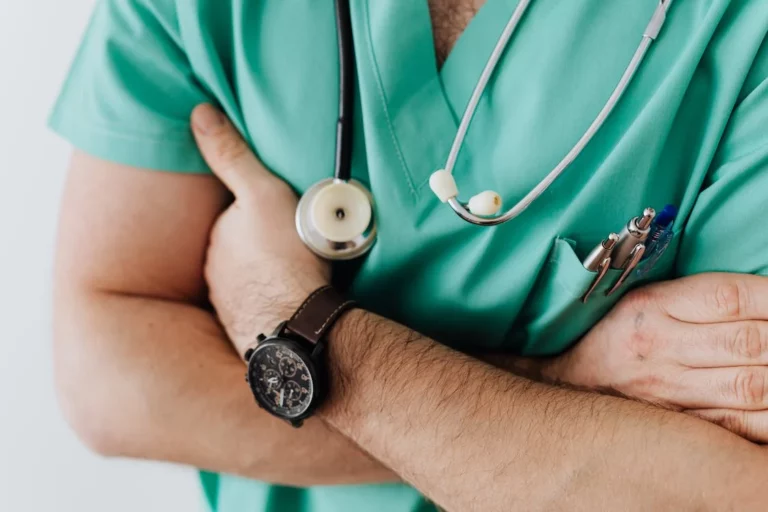 A close up of a doctor's crossed arms with a stethoscope around his neck