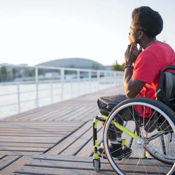 A man using a wheelchair sits on a dock overlooking the water