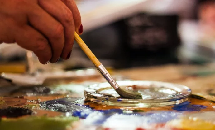 A hand holding a paintbrush dipping it in paints