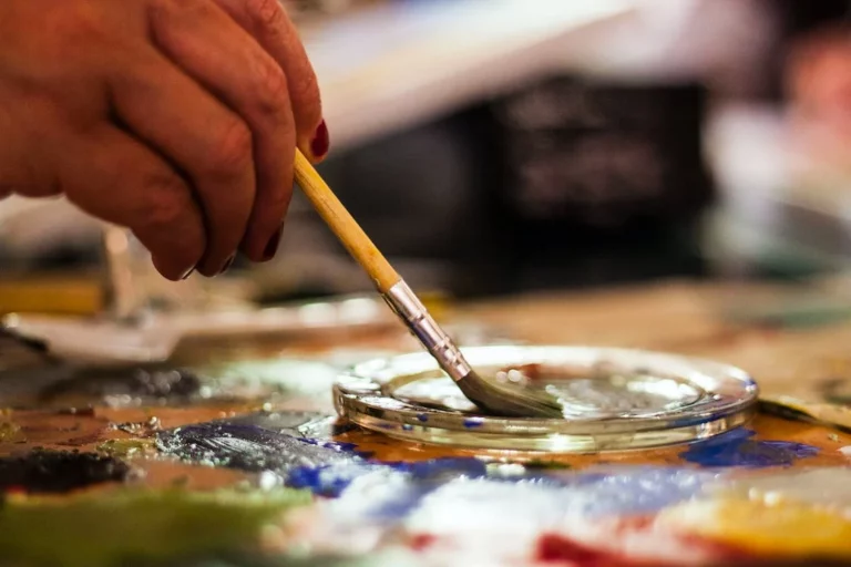 A hand holding a paintbrush dipping it in paints