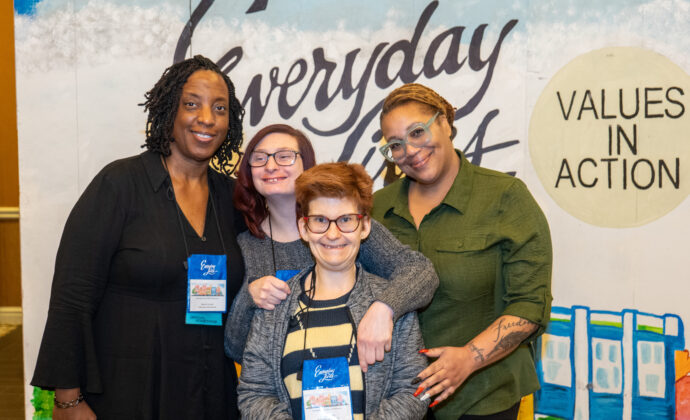 Four people pose in front of the Everyday Lives Conference backdrop