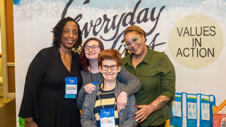 Four people pose in front of the Everyday Lives Conference backdrop
