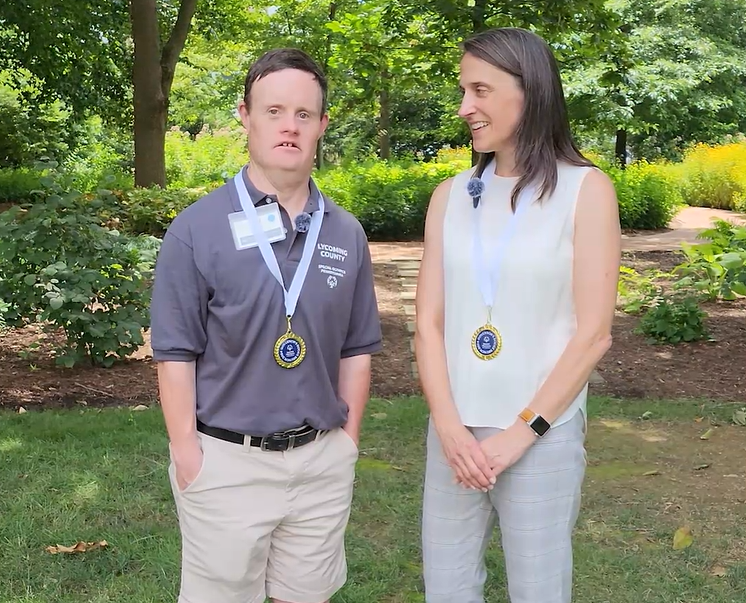 Paul smith and Kristin Ahrens talk in a garden with medals draped around their necks