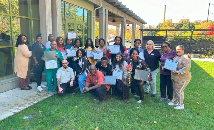 CADES' first class of E-Badge Academy graduates smile while holding up their certificates. 25 people total.