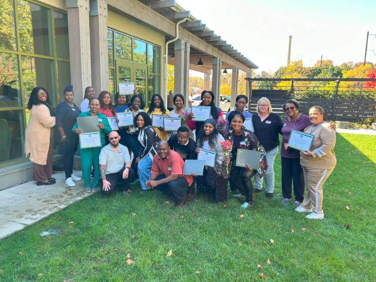 CADES' first class of E-Badge Academy graduates smile while holding up their certificates. 25 people total.