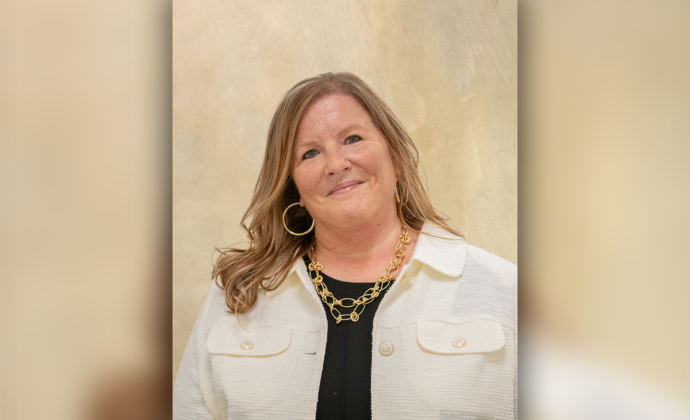 A headshot of Jenn Newell. She is a woman wearing a white blazer, a black shirt, a gold necklace and gold hoop earings. She has dirty blonde hair.