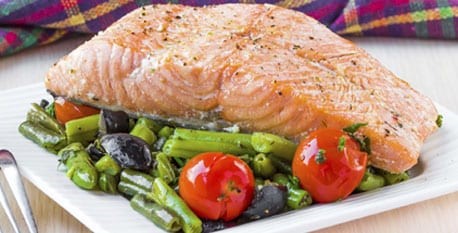 Cooked Salmon sitting on a bed of roasted vegetables - green beans and cherry tomatoes