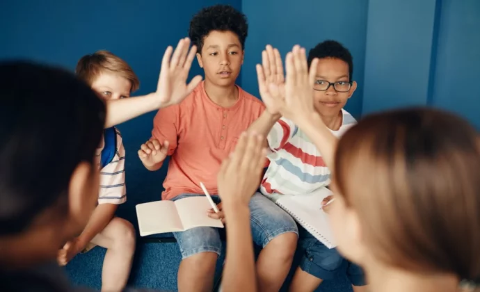 Three children with notebooks in their laps high five two teachers sitting in front of them