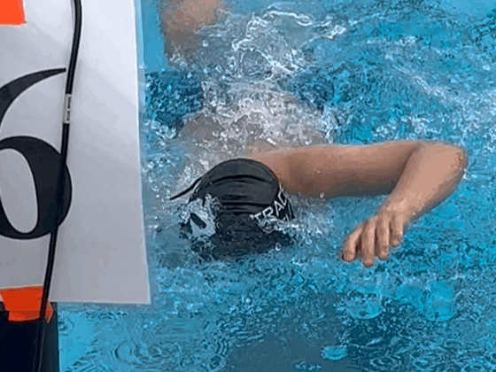 A male swimmer does the freestyle stroke toward the camera in a swim competition. He's wearing a swim cap.