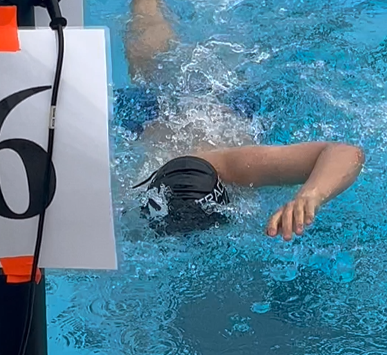 A male swimmer does the freestyle stroke toward the camera in a swim competition. He's wearing a swim cap.