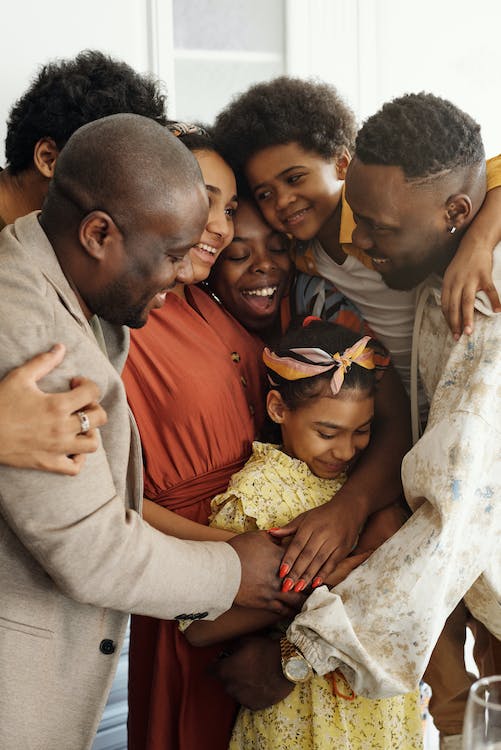 A family embraces in a group hug while smiling. There are two children in the middle of five adults hugging them.