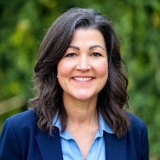 A headshot of Michelle Maikoetter, a professional looking woman with a smile, brown hair, and brown eyes wearing a blue blazer and light blue shirt
