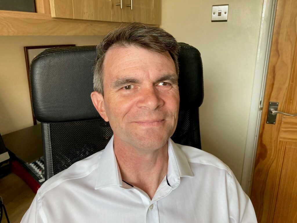 Headshot of Robin Christopherson, a middle age man with brown eyes and salt and pepper short hair styled upward. He is wearing a white button-down shirt.
