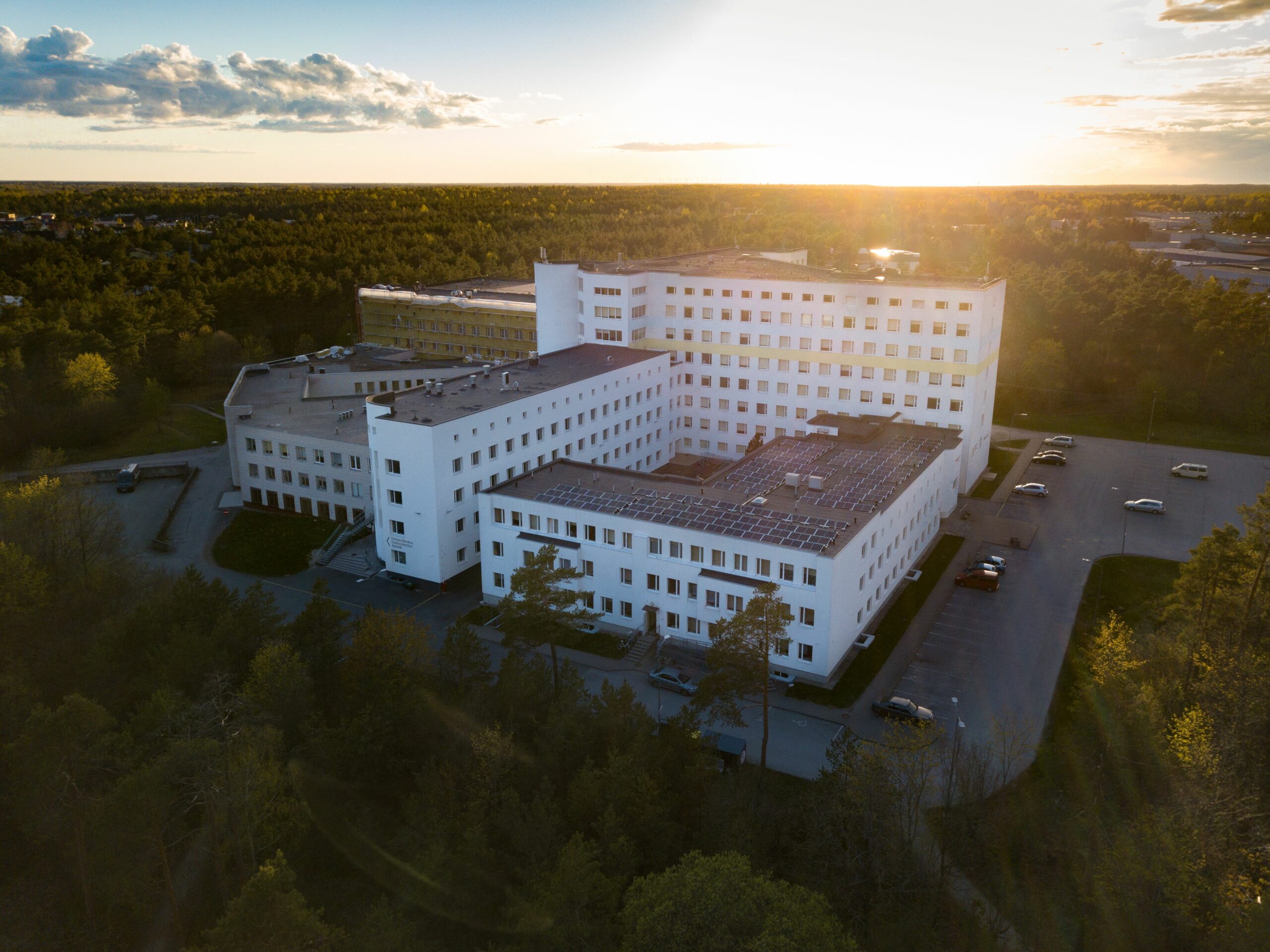 A birds eye view of a hospital surrounded by woods. The sun is peaking over the horizon.
