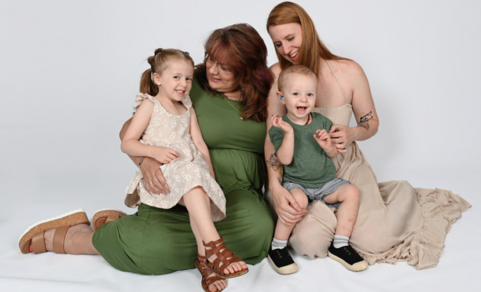 Two women sit on the floor with a young boy and a young girl in their laps. All are smiling wide.