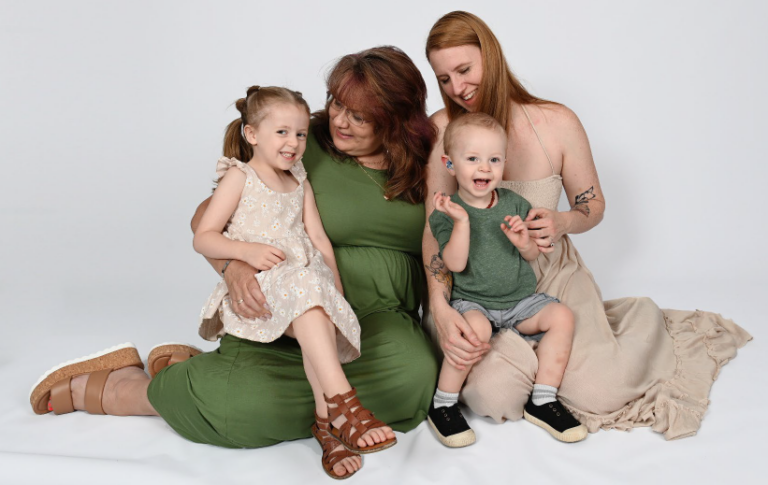 Two women sit on the floor with a young boy and a young girl in their laps. All are smiling wide.