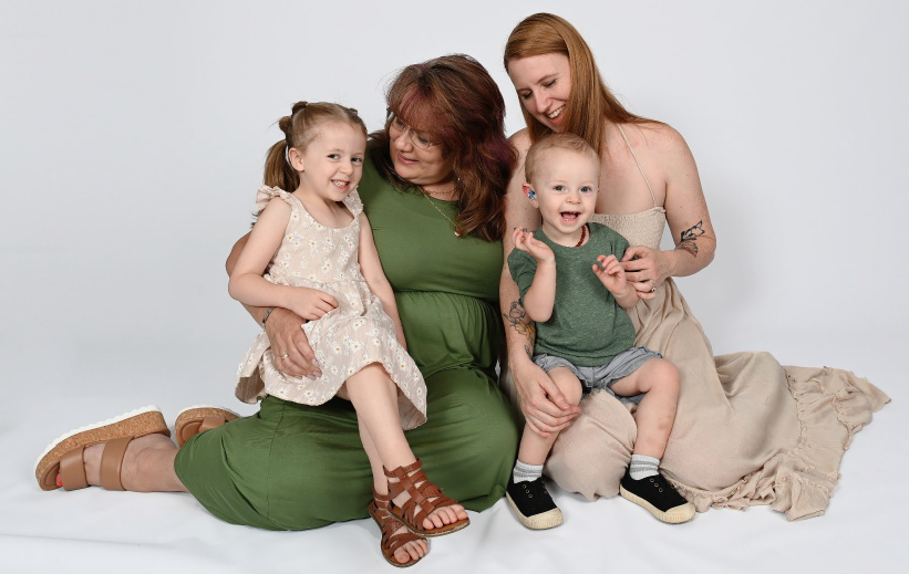 Two women sit on the floor with a young boy and a young girl in their laps. All are smiling wide.